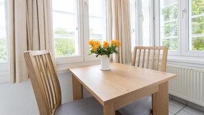 A dining area with a wooden table and chairs, a vase with flowers, and large windows with curtains. - Altes Rathaus Hahnenklee (Goslar)