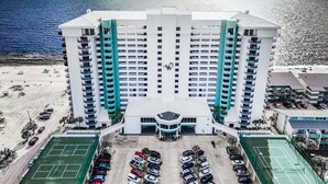 A high-rise hotel with multiple balconies, a central entrance, and a parking lot. - Spectacular 3 Bedroom, 2 Masters on the Water, amazing views, free beach chairs  (Panama City Beach)