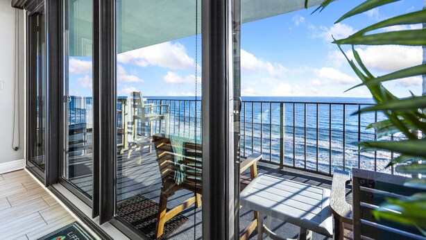 A balcony with a view of the ocean, featuring a wooden bench and a table. - Spectacular 3 Bedroom, 2 Masters on the Water, amazing views, free beach chairs  (Panama City Beach)