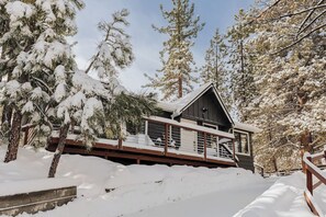 Una cabaña con terraza de madera, rodeada de árboles cubiertos de nieve.