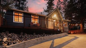 Een houten vakantiehuis met twee verdiepingen, een terras, een stenen fundering en een zonsondergang.