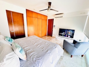 Une chambre à coucher comprenant un lit, une télévision, un ventilateur de plafond et une armoire.