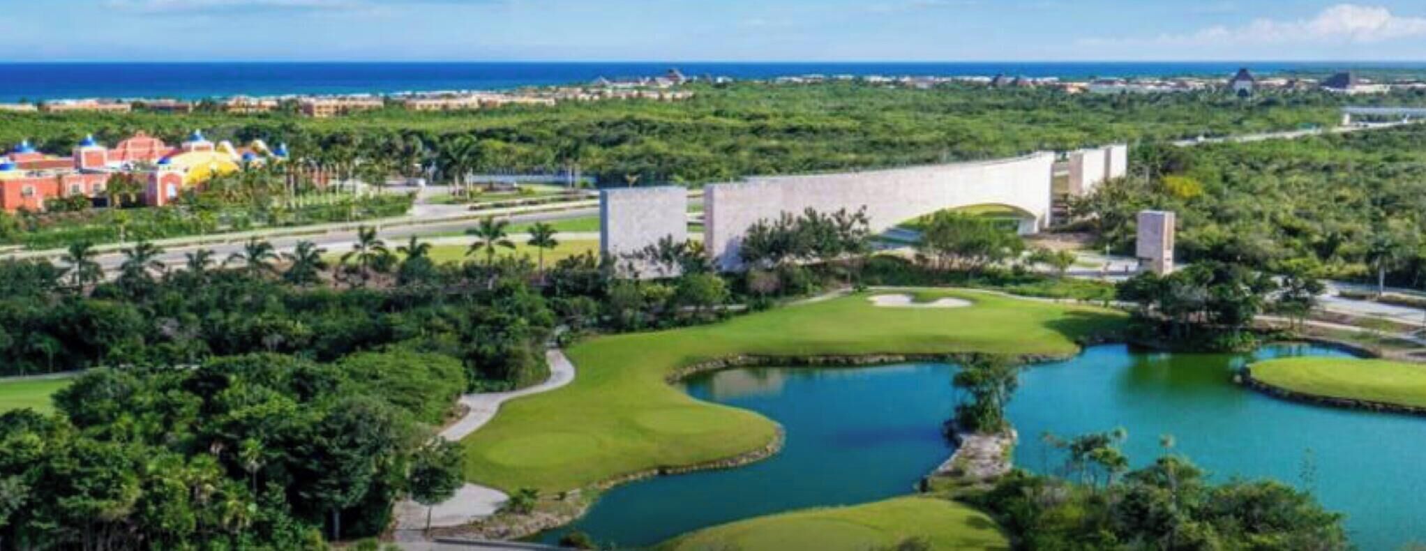 A golf course with a water feature, surrounded by lush greenery and a view of the ocean.