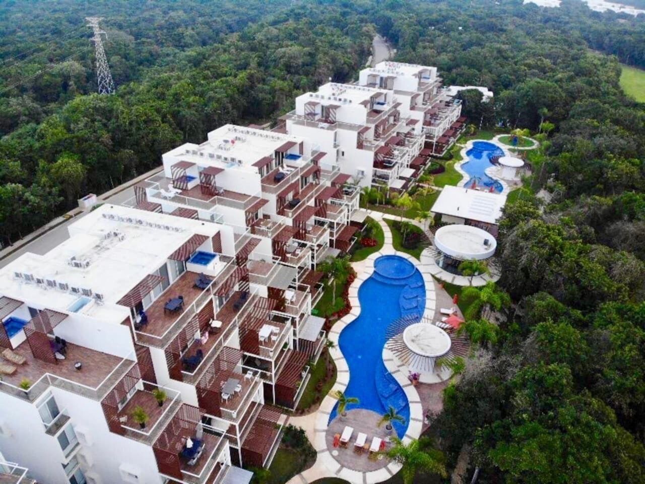 A resort with multiple buildings, a large swimming pool, and a lush surrounding environment.