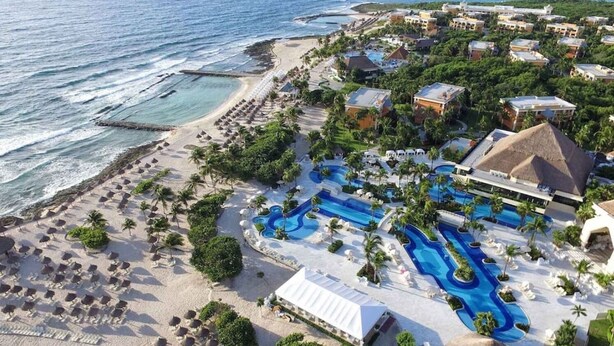 Een luchtend uitzicht op een resort met een strand, meerdere zwembaden en gebouwen van het resort.