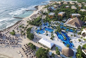 Vue aérienne d’un complexe hôtelier doté d’une plage, de plusieurs piscines et de bâtiments d’hébergement.