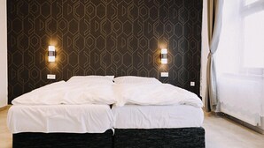 Een bed met witte beddengoed in een kamer met een geometrisch patroon op de muur en twee wandlampen.