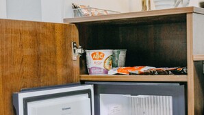 Een compacte koelkast met vriesvak, gevuld met verschillende dranken en een pak melk.