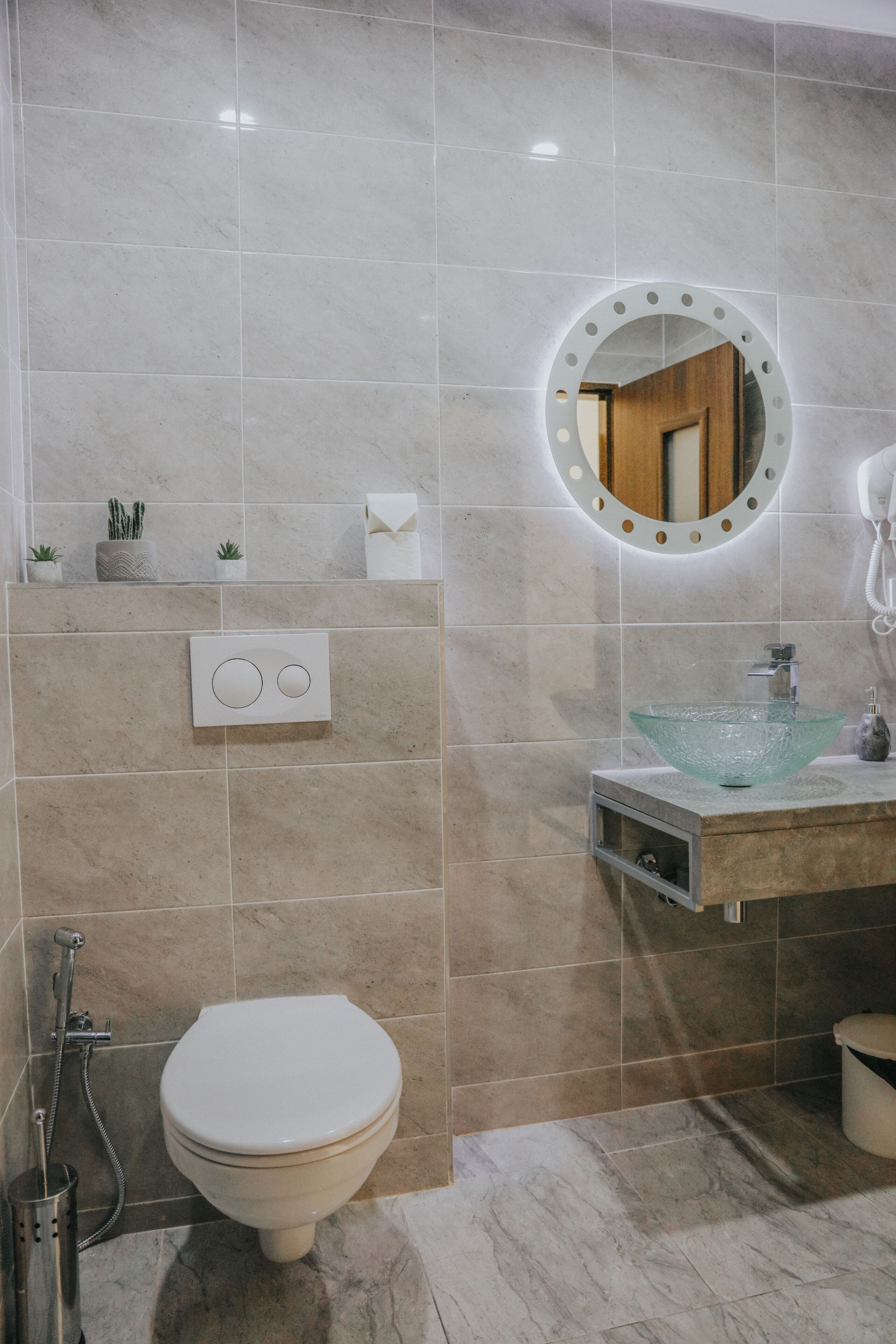 A bathroom with a toilet, a sink with a glass basin, a mirror with a circular frame, and a towel rack.