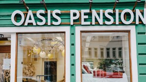 Een winkelgevel met het bord 'OASIS PENSION' en grote ramen die het interieur tonen.