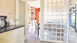 Une cuisine moderne avec des meubles blancs, une machine à café et un coin repas comprenant une chaise et des étagères.