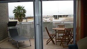 Un balcon avec une table et des chaises, un fauteuil de relaxation et un palmier.