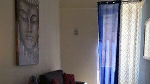 Un salon avec un canapé, une petite table et une chaise. Il y a un tableau au mur et une fenêtre avec des rideaux.