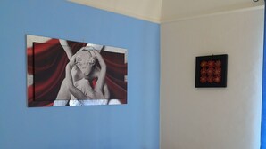 Une chambre à coucher avec un lit, deux oreillers, une table de chevet avec une lampe et des œuvres d’art accrochées aux murs.
