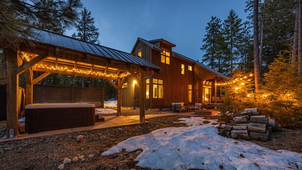 A wooden cabin with a covered patio, a hot tub, and string lights.