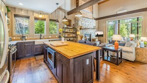 A spacious kitchen with dark cabinetry, a wooden island, and a stone fireplace.