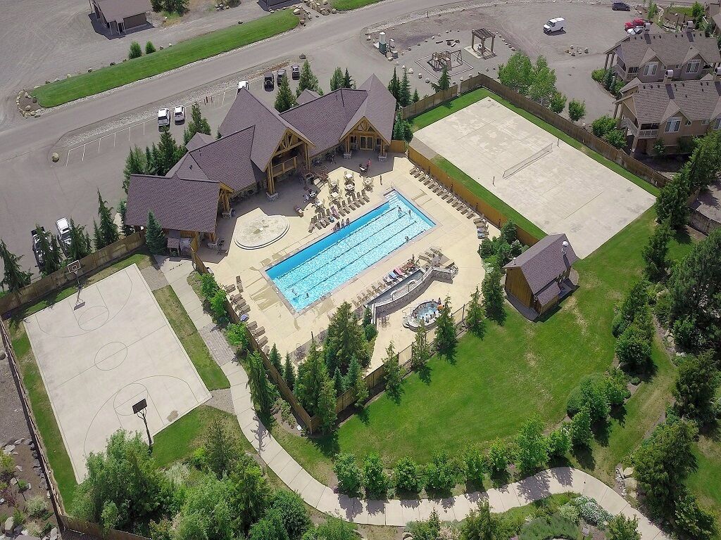 Vue aérienne d’un quartier résidentiel avec une grande piscine, un terrain de basketball et une allée spacieuse.