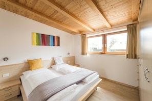 A bedroom with a wooden ceiling, a bed with white bedding, a colorful abstract painting, and a window with curtains. - Weinberg Apartments with Brixen South Tyrol Guest Pass and magnificent views (Raas)