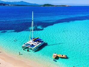 A clear blue sea with a sailboat anchored near the shore.