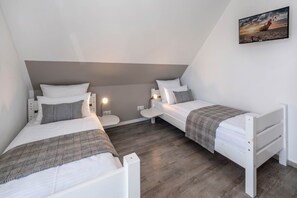 A modern, minimalist bedroom with two single beds, a small bedside table with a lamp, and a wall-mounted TV.