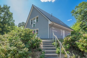 A two-story house with a grey facade, a tiled roof, and a staircase leading to the entrance.