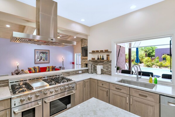 A modern kitchen with a large stove, wooden cabinets, and a view of a pool.
