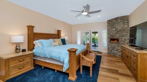 Une chambre à coucher avec un lit, des tables de chevet en bois, un bureau, une cheminée en pierre et un ventilateur de plafond.