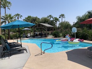 A swimming pool with lounge chairs, umbrellas, and a basketball hoop.