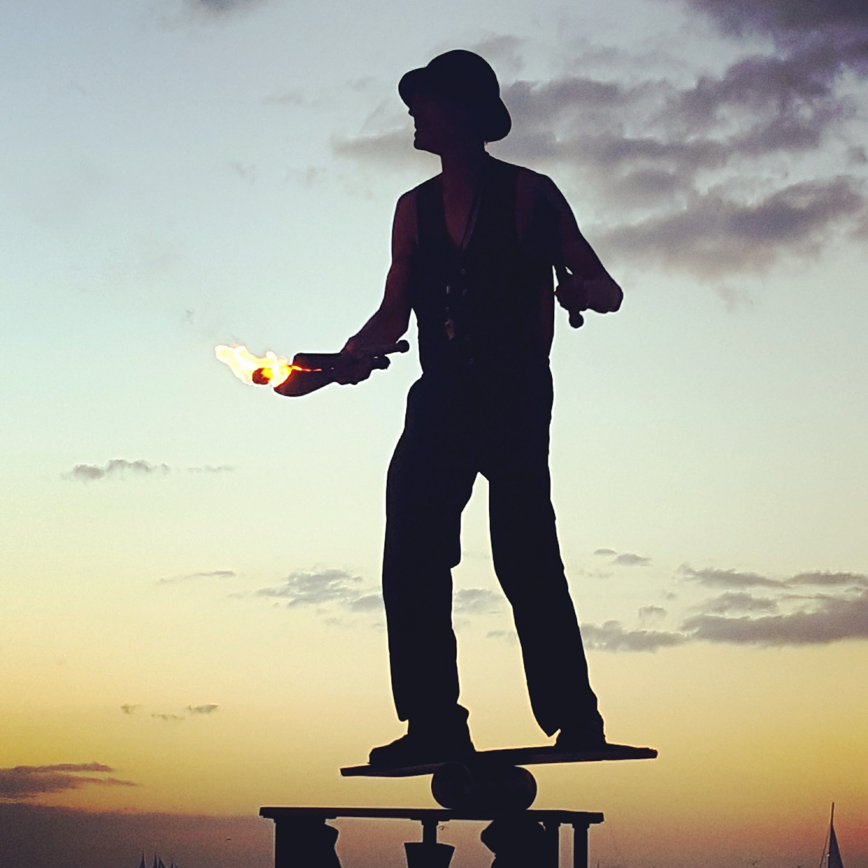 Silueta de una persona sosteniendo una fuente de luz contra un cielo al atardecer.