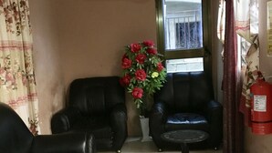 Un salon avec deux canapés en cuir noir, une petite table ronde, une plante en pot aux fleurs rouges et une fenêtre donnant sur un beau paysage.