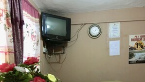 Une pièce avec un comptoir d’accueil en bois, un téléviseur fixé au mur et un panneau d’affichage où sont accrochées des annonces.