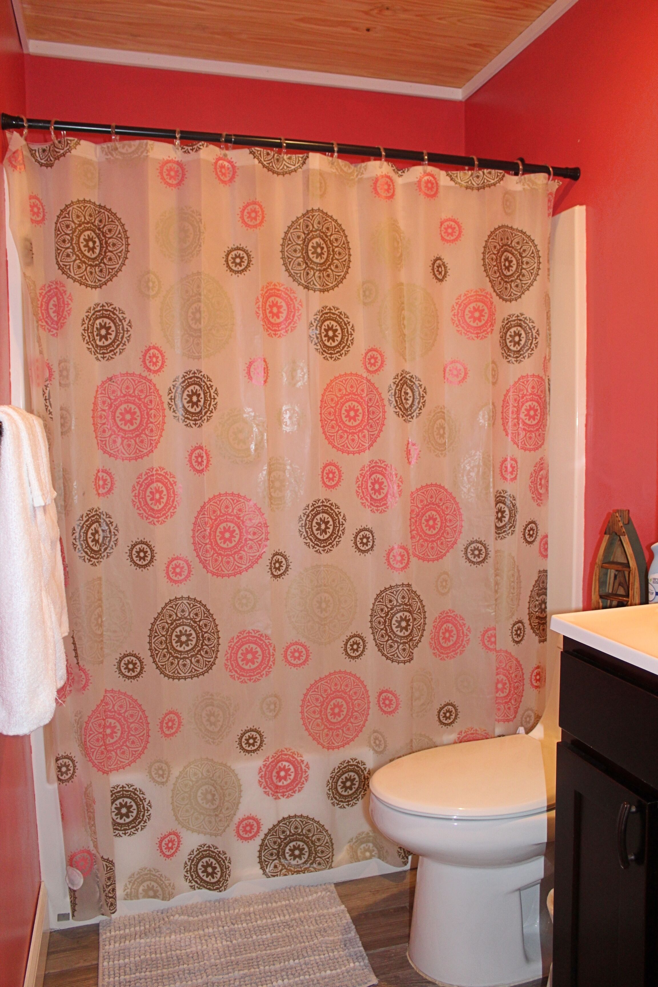 A bathroom with a patterned shower curtain, a white toilet, and a wooden floor.