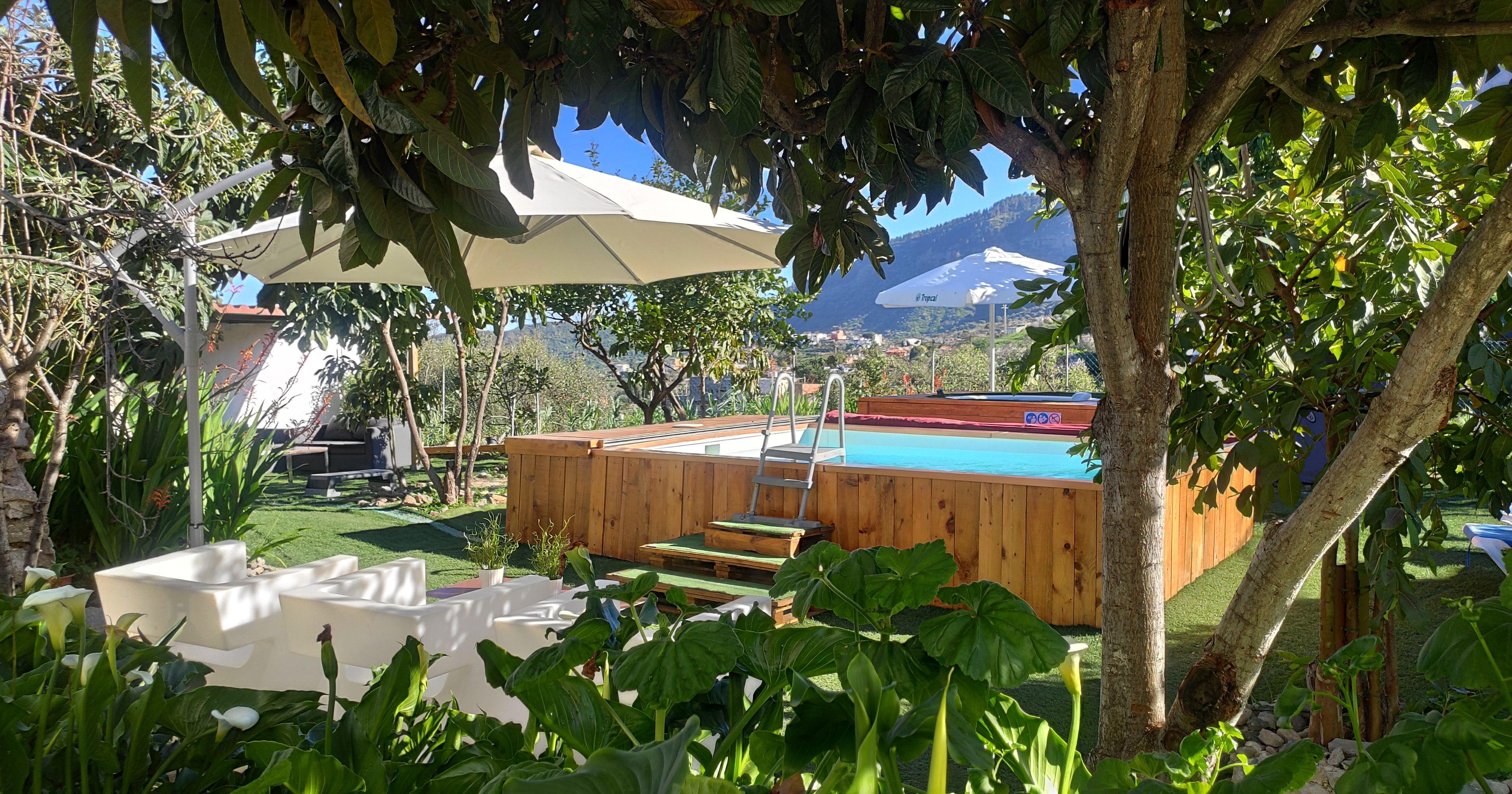 Un jardin avec une terrasse en bois, une piscine et un espace salon abrité.