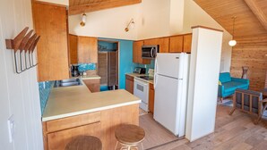 A compact kitchen with wooden cabinets, a microwave, a refrigerator, and a sink. There are two stools and a small table. The ceiling has exposed wooden beams. - hot tub, ocean views and wood burning fireplace (Tillamook)