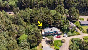 An aerial view of a house surrounded by dense forest, with a visible driveway and parked cars. - hot tub, ocean views and wood burning fireplace (Tillamook)