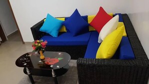 Una sala de estar con un sofá azul, un sillón de mimbre negro y una mesa de centro de vidrio con un centro de mesa floral.