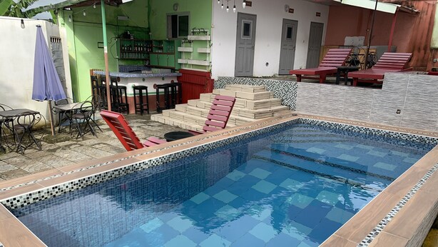 Una piscina rectangular con bordes de azulejos, rodeada por una terraza de madera y mobiliario exterior.