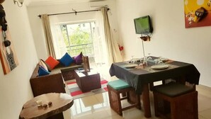 Un comedor con una mesa lista para cuatro personas, un televisor montado en la pared y una ventana con cortinas.