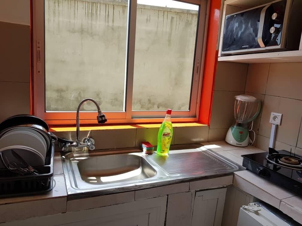 A kitchen with a stainless steel sink, a dish rack, a window with a view, and a blender on the countertop.