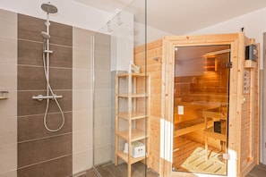 A modern bathroom with a shower, a glass-enclosed sauna, and wooden shelves. - Cozy vacation apartment in Loddin with garden, sauna and playground near the east (Loddin)