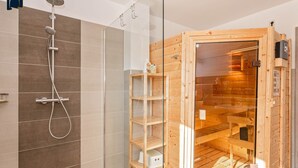 Une salle de bain moderne avec une douche à parois de verre, des étagères en bois et un sauna.