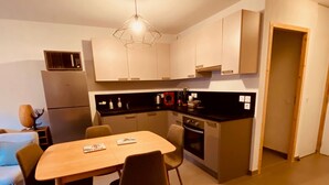 Una cocina compacta con una mesa de comedor, sillas, un refrigerador, un microondas y una lámpara colgante.