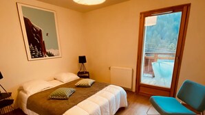 Un dormitorio con cama, una silla, un radiador, una ventana y un cuadro en la pared.