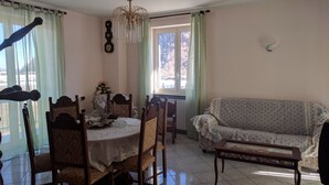 Ein Essbereich mit Tisch und Stühlen, einer Chandelier, einer Couch und einem Fenster mit Vorhängen.