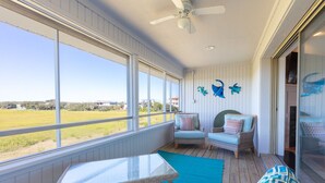 A sunlit room with large windows, wicker furniture, and a ceiling fan. -  Summer in Vilano Beach, St. Augustine with awesome Sunsets (St. Augustine)