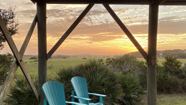 A wooden deck with two turquoise Adirondack chairs facing a sunset over a grassy landscape. -  Summer in Vilano Beach, St. Augustine with awesome Sunsets (St. Augustine)