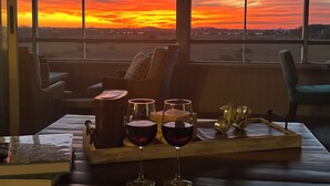 A cozy room with a large window overlooking a sunset. Inside, there is a wooden table with a tray holding glasses of red wine and a vintage radio. -  Summer in Vilano Beach, St. Augustine with awesome Sunsets (St. Augustine)