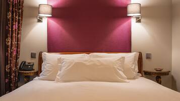 Une chambre d’hôtel avec un grand lit, deux lampes de chevet, un téléphone, une petite table avec un bol, et un rideau décoratif.