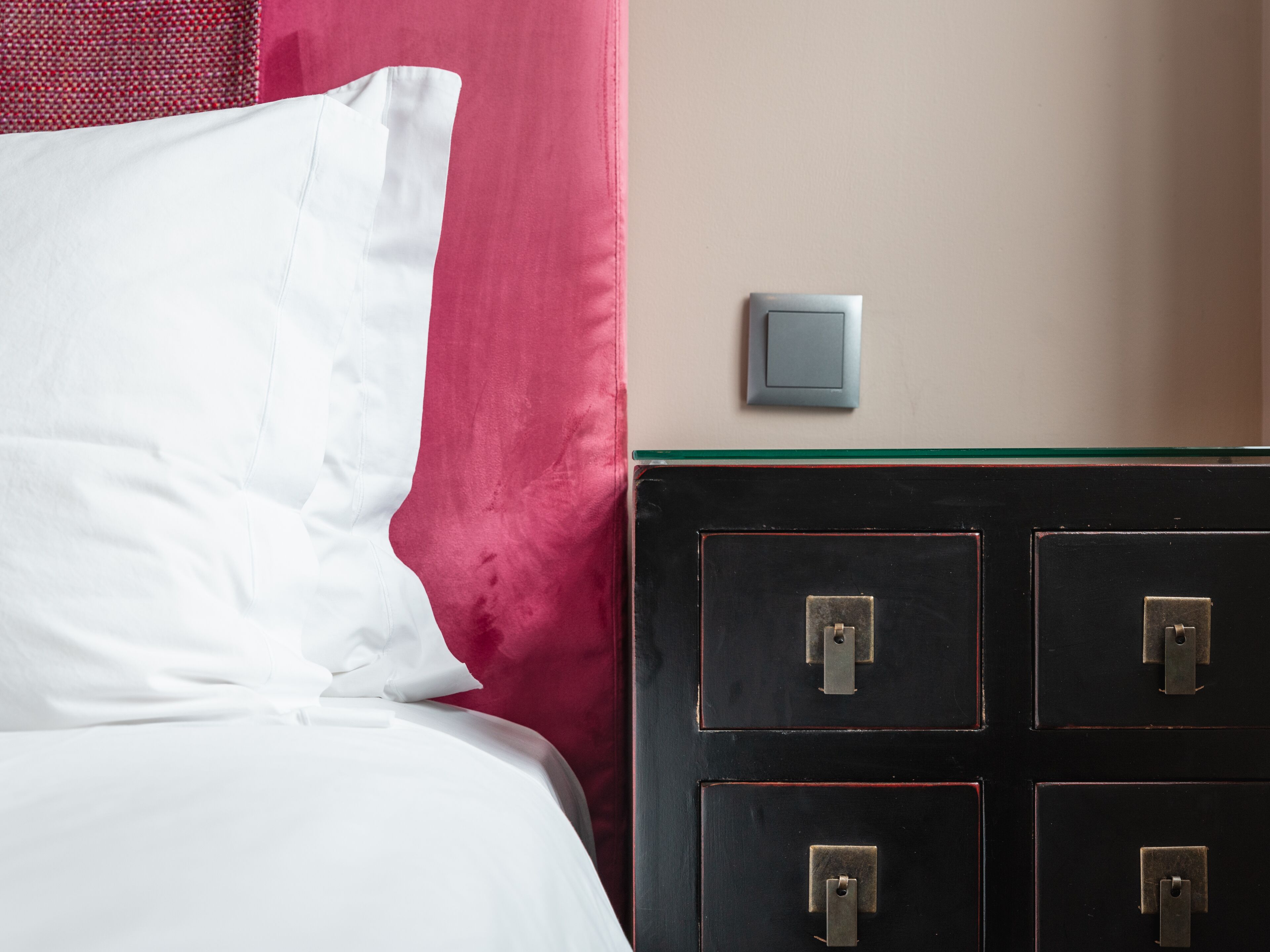 A bed with white linens, a red curtain, and a black dresser with drawers.
