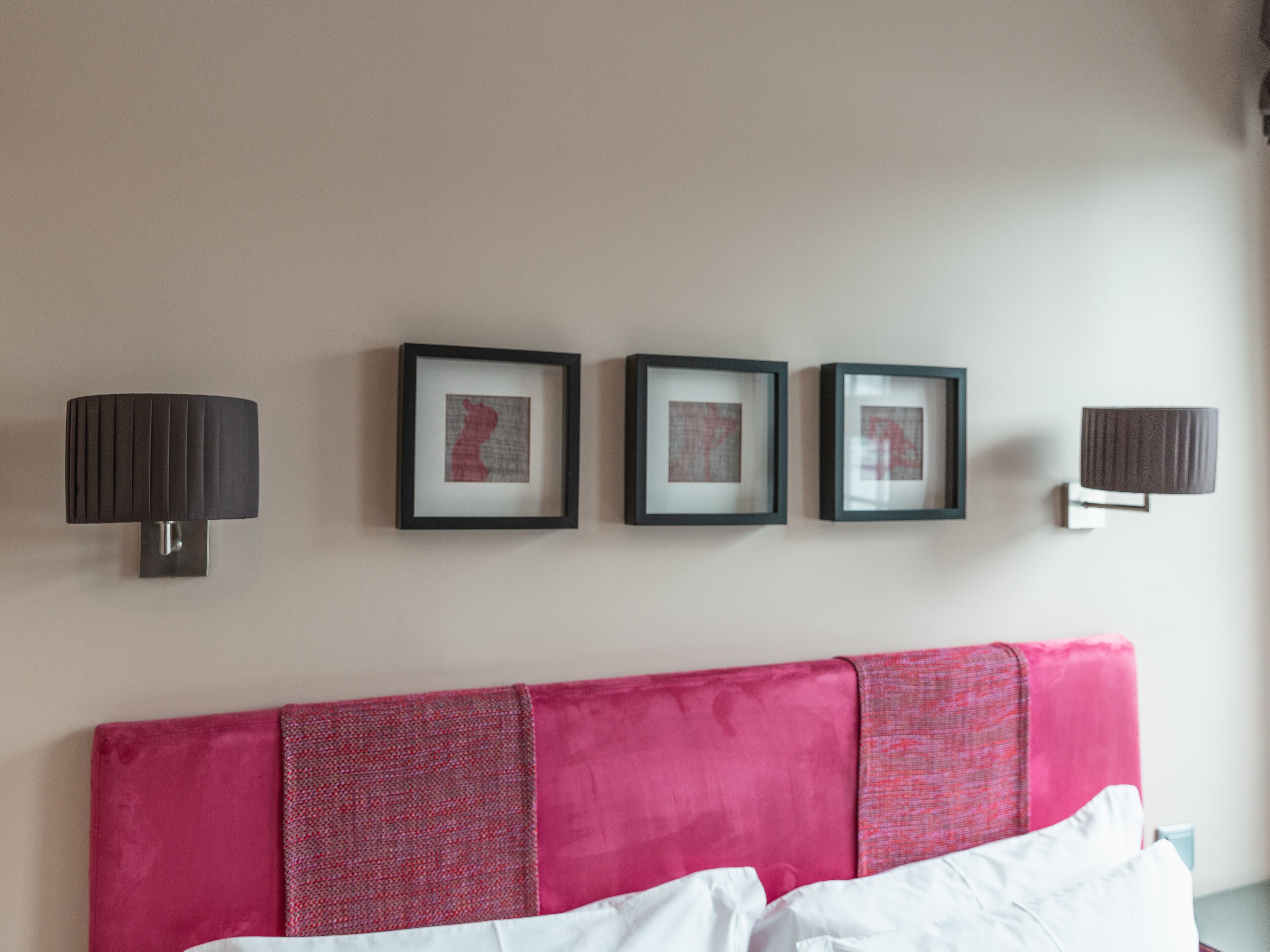 A bedroom with a bed, a headboard, and four framed artworks on the wall.